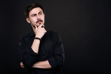 Pensive handsome young man in black shirt touching chin while brainstorming about idea