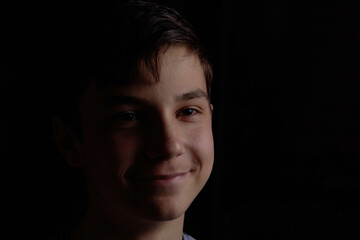 Portrait of a teenager on a black background. The boy has dark hair