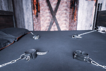 Torture of Andreev cross on the bedroom wall. VDSM equipment and sex toys. Leather handcuffs with a chain on a gray sheet. The lashes hang in the room for perversions.