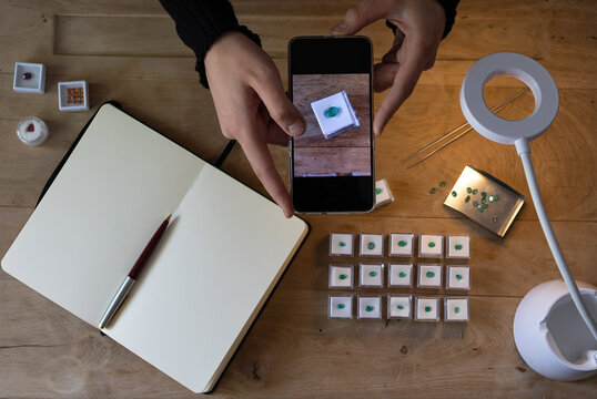 Gemologist working taking photos of precious emerald stones with her mobile phone. Top view of a gemologist work space.