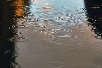 Drops of rain bubbling in a puddle with the reflection of light