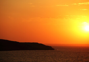 Beautiful scenic landscape with going down sun and dramatic colorful sky at sunset time and silhouette of black cape at foreground in Taman, Krasnodar Krai, Azov sea, Russia