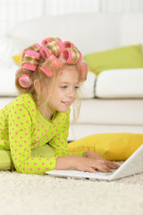 Lovely little girl with pink curlers using laptop