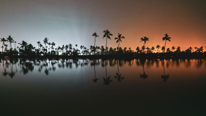 Kerala tourist model village kumbalanghi at night with warm light on one side and cool lighting on the other with reflections in the backwater