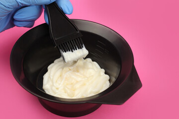hair dye is mixed by a gloved hand in a bowl on a pink background