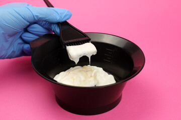 hair dye is mixed by a gloved hand in a bowl on a pink background