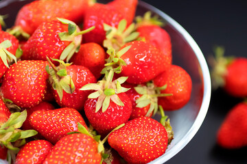 Fresh organic strawberries in a glass bowl  on a black table.