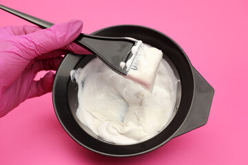 hair dye is mixed by a gloved hand in a bowl on a pink background