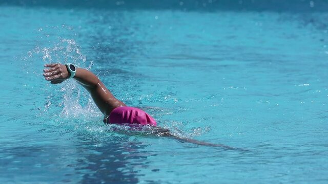 footage of a female swimmer swimming laps in an outdoor pool using the freestyle stroke as part of her triathlon training plan