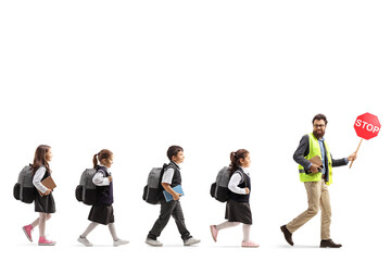 Male teacher in a safety vest walking with a stop sign and schoolchildren following behind