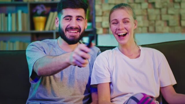 Happy and smiling couple at home watching tv in front of the camera they discussing about some movie and enjoying the time