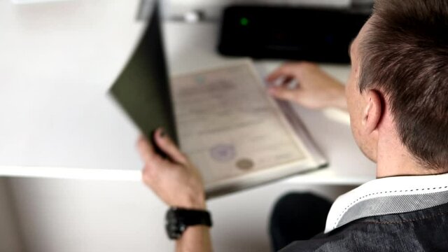 The man opens a black folder and looks at the documents in it. Subordinate worker brought the file with documents to boss, blur video in slow motion. Boss is sitting back to camera.