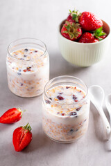Granola breakfast in glass jars with yogurt or milk on gray cement background