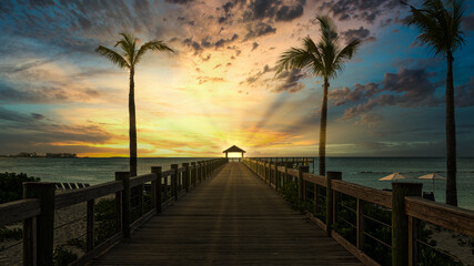 beautiful sunset at the wooden jetty at the beach with palms. 
