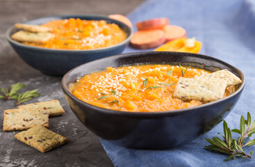 Sweet potato or batata cream soup with sesame seeds and snacks in blue ceramic bowls on a black concrete background. side view, selective focus