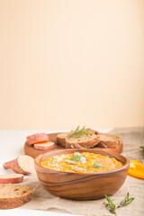 Sweet potato or batata cream soup with sesame seeds in a wooden bowl on a white wooden background. side view, selective focus.