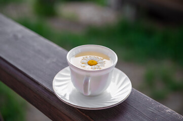 Green tea in a white mug with a chamomile inside on a brown wooden background