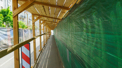 Protective canopy over the sidewalk and fence near a house under construction.