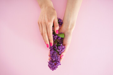 Beautiful female hands and a branch of lilac on a pink background. Beautiful manicure, flat lay. Beauty and skin care concept