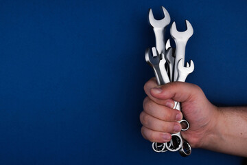 Set chrome spanner keys in mans hand on blue background. Flat lay, top view, minimal composition with copy space.