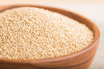 Wooden bowl with raw white quinoa seeds on a white wooden background. Side view, selective focus.