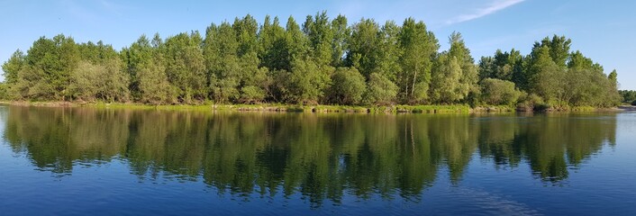 Obraz premium Beautiful scenery of a range of green trees reflecting in the lake