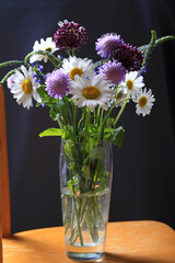 Bouquet of beautiful multi-colored wildflowers in a glass vase on a dark background