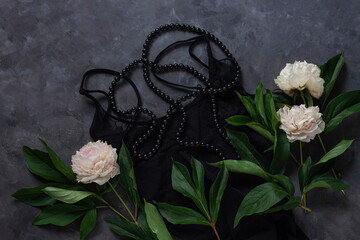 Woman's glamour black lingerie and jewelry accessories with white peony flowers on dark background. Female fashion blog flat lay social media copy space. Lace underwear sexy combine clothes top view.