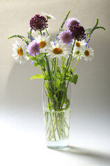 Bouquet of beautiful multicolored wildflowers in a glass vase on a light background