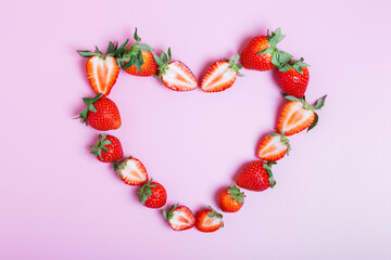 Obraz premium Frame in the shape of a heart made from ripe strawberries on a lilac background. Love concept. Valentine's day concept. Beautiful background for the designer. border, flat lay, copy space.