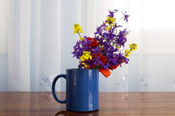 Drinking ceramic cup full with a small bouquet made from different field flowers.