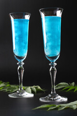 Shimmer edible glitter sparkling blue wine in two tall glasses on black background. Vertical format. Closeup.