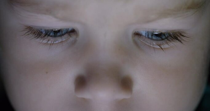 Detail of blue eyes child portrait looking at tablet screen, lost childhood, technology, close up