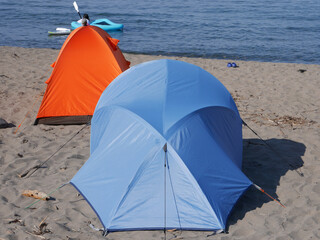 Camping tents on a sunny beach behind the blue sea and sky