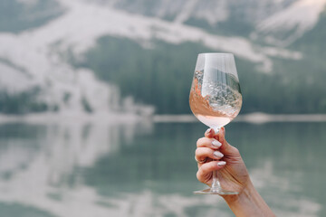 The hand pf you ng lady with a glass of wine on Lake Braies shore with a green forest on the...