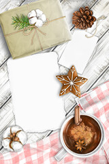 Hand drawn winter mock-up scene. Blank cotton paper greeting card, tag, craft gift box, wooden background, hot chocolate, fabric, gingerbread star, pinecone. Top view.