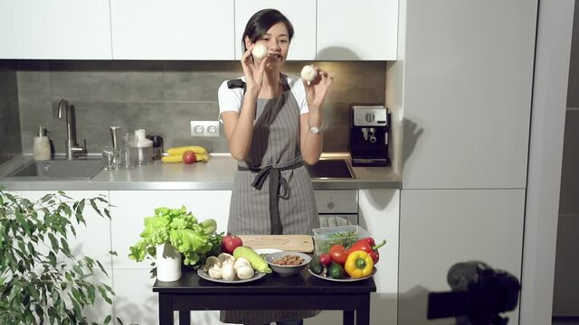 Attractive young woman recording a video about healthy eating on digital camera in the kitchen at home. Vlogging and social media concept.