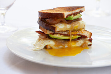 Toasted egg, bacon, and avocado sandwich, cut and stacked with egg yolk running onto plate