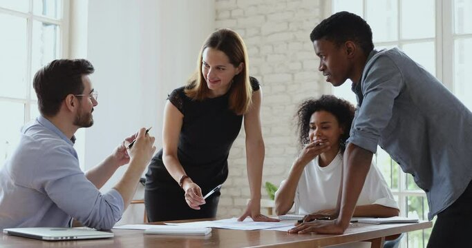 Happy female manager executive and multiracial team people analyze paperwork talking laughing working together share ideas in teamwork discuss project plan at office table at group corporate meeting