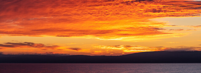 Amazing panorama. Scenic red-and-orange sunset with a shoreline as a silhouette in the foreground.