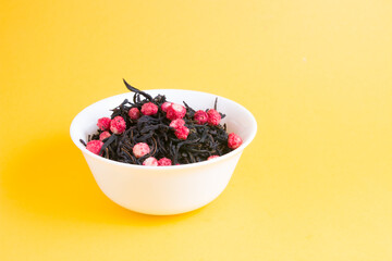 heap of tea with dried strawberries in a small white bowl on a yellow background