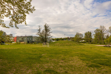 Fototapeta na wymiar Beautiful landscape view of football goal on green grass lawn. Modern village houses and tall green trees on cloudy sky background. Sweden. Europe.