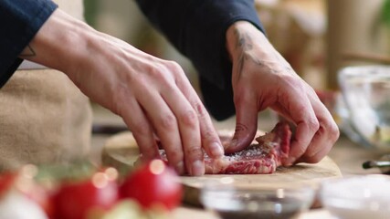 Close up shot of hands of professional male chef adding salt to raw meat steak and flipping it to the other side while preparing it for cooking
