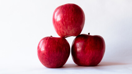 Plano frontal  de tres manzanas rojas y frescas completamente aisladas sobre un fondo blanco y con iluminación natural sobre ellas