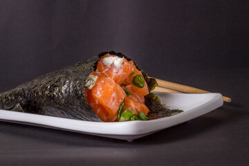 Salmon temaki sushi on white plate in black background