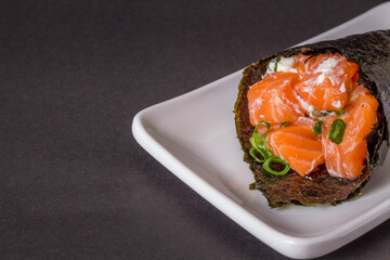 Salmon temaki sushi on white plate in black background