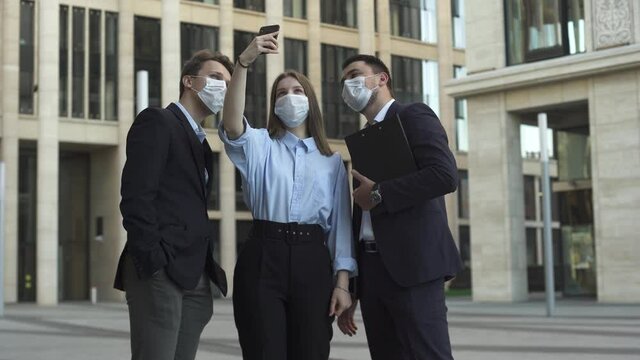 Businesswoman in a formal suit take selfie with her colleagus businessmen on the street near modern office building during pandemic covid-19 coronavirus quarantine. Business is opening after lockdown.