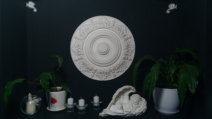 Gypsum alabaster round classical wall decoration rosette, some candles, plants and sculpture of angel. © kalyanby