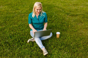 Top view of woman sitting in park on the green grass with laptop, hands on keyboard. Computer screen mockup. Student studying outdoors. Copy space for text