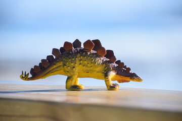 Dinosaur toy standing outside with the beach and ocean in the background. © CarlyZel